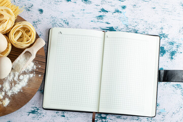 Tagliatelle with oil, egg and flour on wooden board and notebook