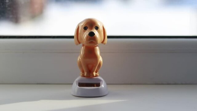 natural light. a brown toy dog stands on a white window and shakes its head. Powered by the sun