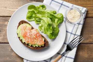 Whole grain rye bread toast with salmon and avocado on wooden table background. Flat lay, top view