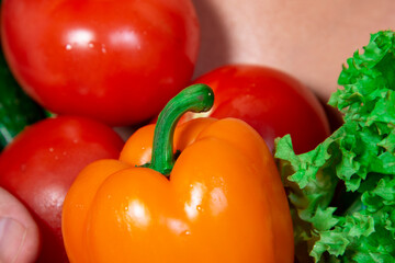 A beautiful male body and natural vegetables. Diet and nutrition. Orange background. Broccoli, tomatoes, cucumbers, peppers and lettuce.
