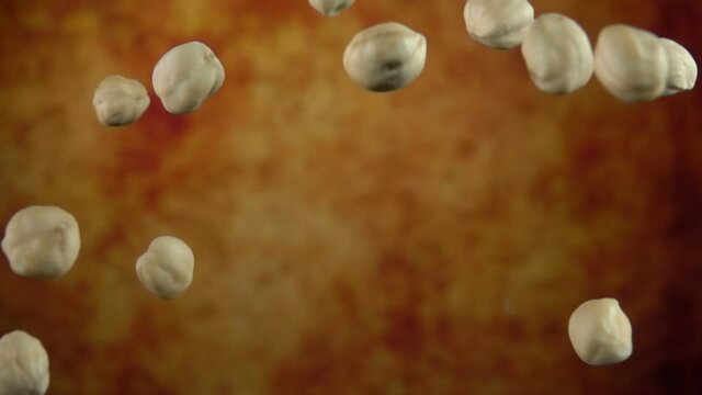 Super close-up of peeled hazelnuts bouncing on a yellow ochre background in slow motion