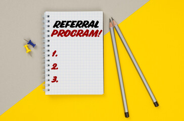On a yellow-gray background are pencils, buttons and a notebook in which it is written - Referral Program
