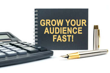 On a white background, there is a calculator, a pen and a black notebook with the inscription - GROW YOUR AUDIENCE FAST