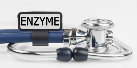 On the white surface lies a stethoscope with a plate with the inscription - ENZYME