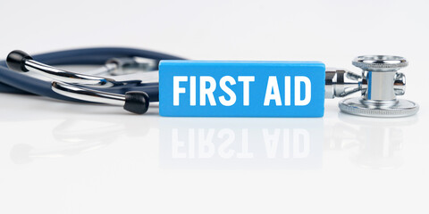 On a white reflective surface is a stethoscope and a blue Jenga with the inscription - FIRST AID