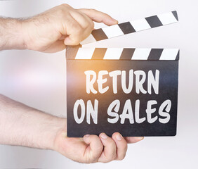 On a white background, a man holds a clapperboard in his hands on which it is written - RETURN ON...