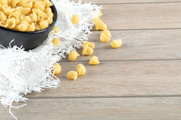 Bowl of dry pasta on wooden table with burlap
