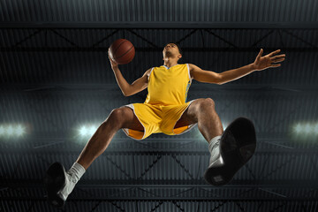 Young professional basketball player in action, motion isolated on black background, look from the...