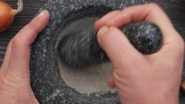 Close-up top view of pestle mixing spices in the grey stone mortar on the dark wooden surface