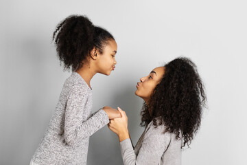 African american mother with her daughter looking at each other on neutral grey background.