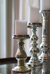 Classic sparkly silver gold candle holders arranged on the glass table. Interior design. Decorating  with candles concept.