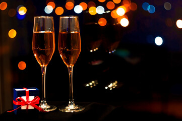 two glasses of pink champagne with a gift box for jewelry against the backdrop of the lights of the night city. High quality photo
