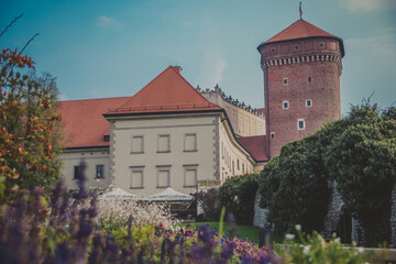 Wawel Senator Tower with castle, green lawns, ivy on the wall, umbrellas and flowers on sunny day. Part of the Wawel royal Castle in Krakow, Poland. Built at the behest of King Casimir III the Great. 
