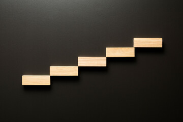 Wooden tiles form a stairway with copy space on a black background