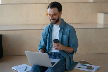 Young handsome man wearing stylish eyeglasses working freelance project, searching online. Smiling...