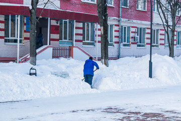 Snow removal. A worker removes snow with a shovel after a snowfall on the sidewalk.