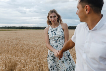 Young couple holding hands and walking on the wheat fild. Love story.