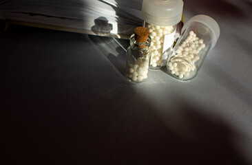Homeopathic granules in storage flasks. In the background, a book on homeopathic treatment.
