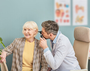Positive elderly woman while ear examining at a hearing clinic. ENT Doctor checking elderly patient...