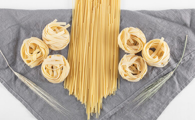 Raw tagliatelle and spaghetti pasta on gray tablecloth