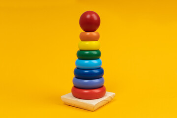Multicolored wooden toy pyramid on yellow background. Toy, build from colored wooden rings