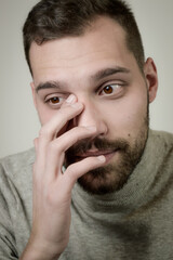 Fototapeta premium Portrait of a young man with a short beard who in a moment of emotion touches his eye