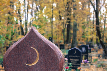 Golden muslim crescent moon on a granite tombstone. Islamic grave with half moon in the autumn cemetery