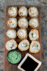 Fried hot sushi rolls on a wooden board with wasabi and soy sauce
