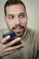 Portrait of an amused young man who is recording an audio message on his smartphone