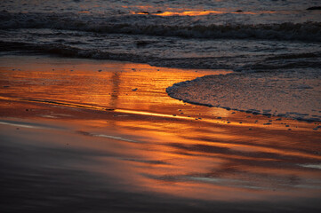 Shoreline of the sea with orange reflection of sunset sky