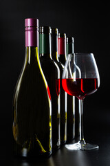 several different bottles of wine and a glass with red wine on a dark glossy background.