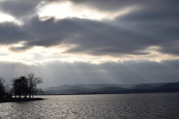 sun through clouds over lake