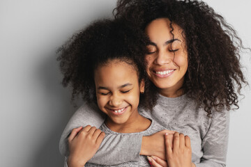 Happy african american mom and her little daughter smiling and embracing with eyes closed.