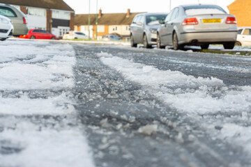 Dangerous Road Conditions with Packed Ice on the road with a layer of Snow and Cars Parked up at the roadside in a Housing Estate. © Stephen Dewhurst