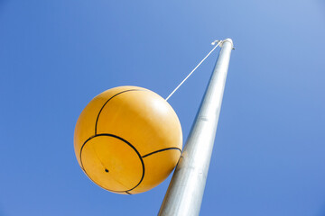 A view looking up at a tetherball attached to a metal pole, against a blue clear sky.