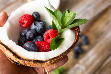 A closeup view of a hand holding a half coconut filled with mint and assorted berries.