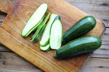 Sliced zucchini on a round wooden cutting board. Close-up of fresh young squash with water drops....