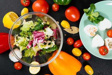 salad with vegetables. Different vegetables for salad on a black background. Salad in a transparent bowl. Salad of tomatoes, peppers and lettuce. 