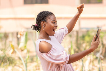 african lady feeling excited and happy looking at her phone