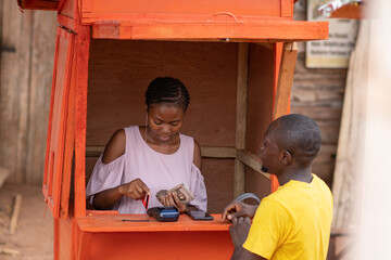 nigerian lady in a kiosk attending to a man who wants to withdraw money from a pos service instead...