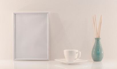 Modèle de cadre photo blanc avec espace vide pour logos, inscription publicitaire. Cadre en mode portrait sur un espace de travail avec un vase et une tasse à café.