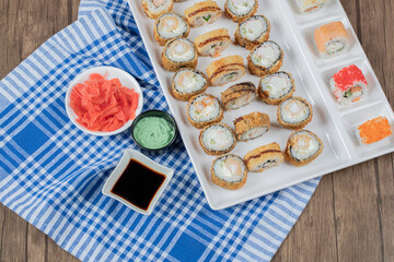 Hot sushi rolls on a wooden platter with soy sauce, ginger and wasabi