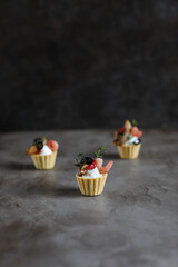 Canapes with curd cheese and seafood on a wooden board. Small snacks on a dark background.