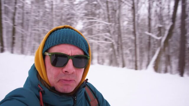 An active blogger with glasses holds a camera in his hands while running. Films himself for subscribers, winter active games. Runs, gestures, faces. Shaking the camera.