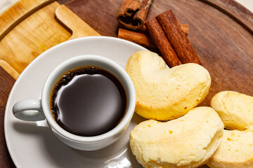 Xícara de café com biscoito de queijo e pau de canela sobre a mesa.