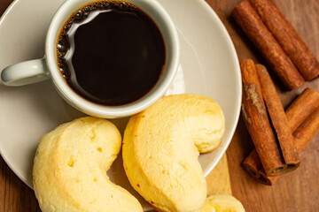 Xícara de café com biscoito de queijo e pau de canela sobre a mesa.