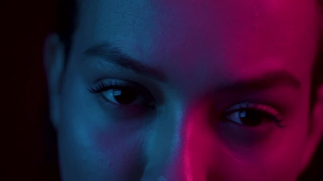 Female eyes blinking under neon blue pink light. Girl's beautiful face with long lashes. Nightlife, night club concept