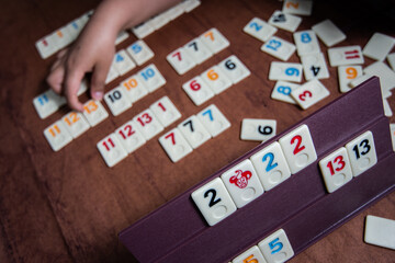 Kid playing Rummy with game tiles laid on a plastic rack simulating wood, in a mosaic style
