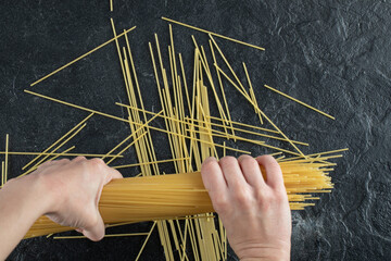 Woman hands breaking spaghetti on dark background