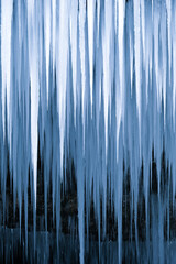 Beautiful long icicles of a frozen waterfall, with water flowing and crashing down and Ice water dripping from the tips of icicles in a cold eery and moody atmosphere in a cave in the mountains 
